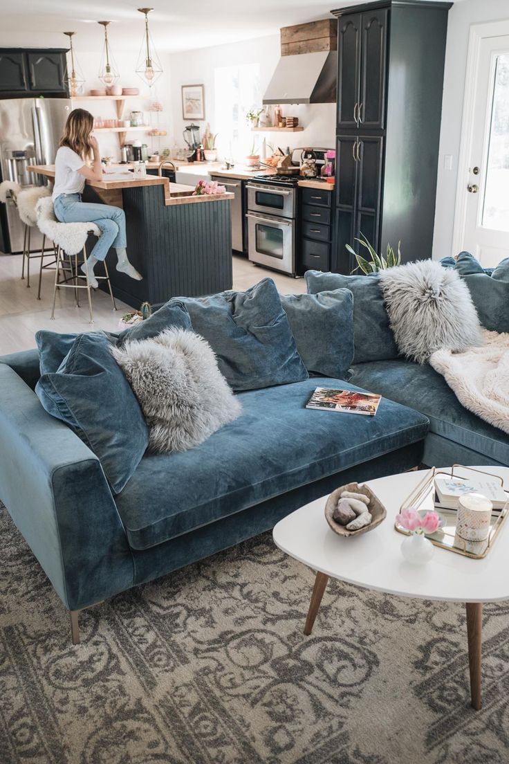 a living room filled with furniture and a woman sitting at a kitchen counter in the background