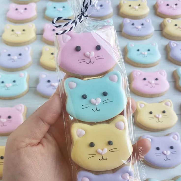 a person holding three decorated cookies in front of a bunch of cats on a table