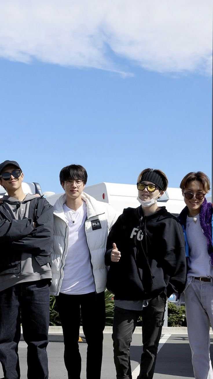 four young men standing next to each other in front of a building with a plane behind them