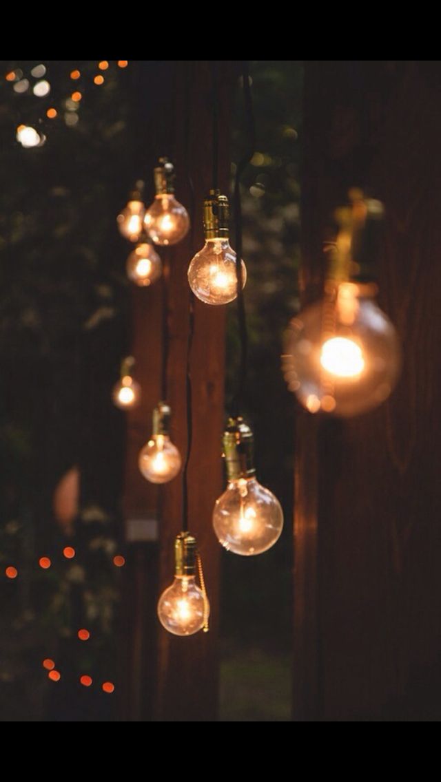 several light bulbs hanging from a wooden fence with lights in the dark behind them and blurry background