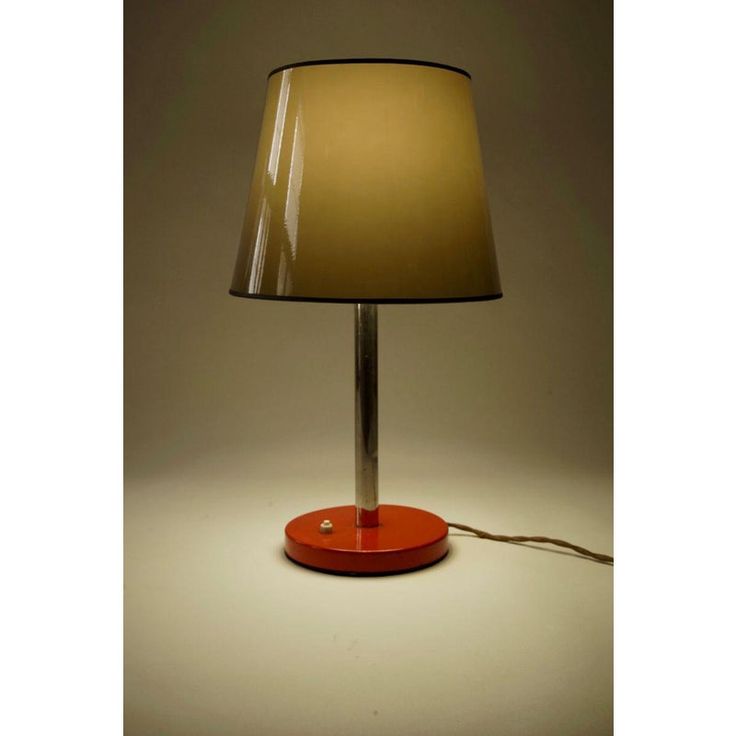 a lamp that is sitting on top of a table with a red base and a beige shade