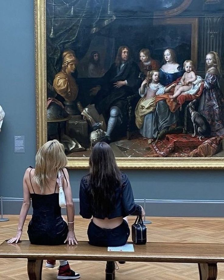 two women sitting on benches in front of a painting with people looking at it and writing