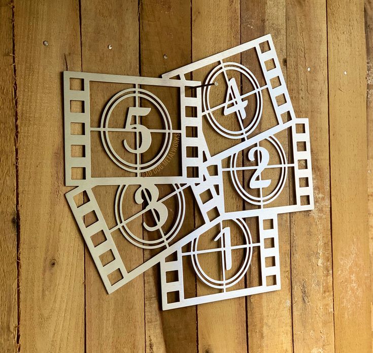 four pieces of paper cut out with numbers and symbols in them on a wooden surface