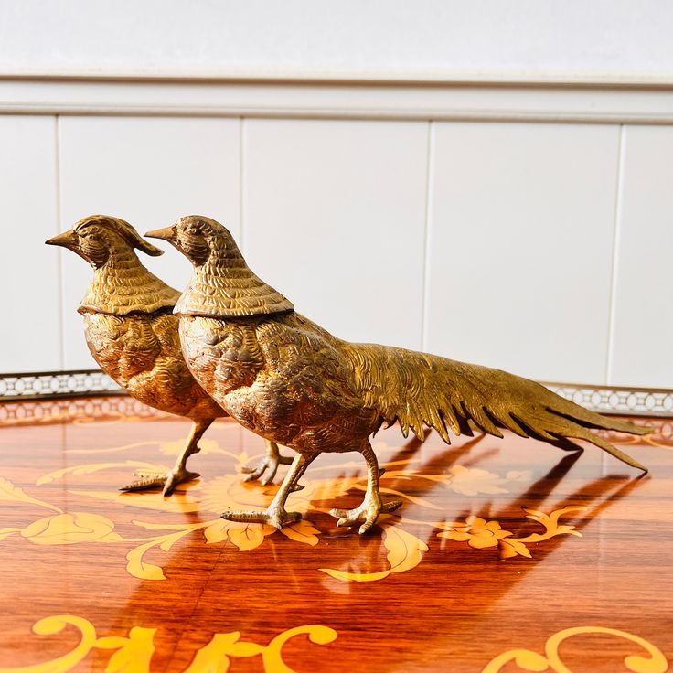 two brass birds standing on top of a wooden table