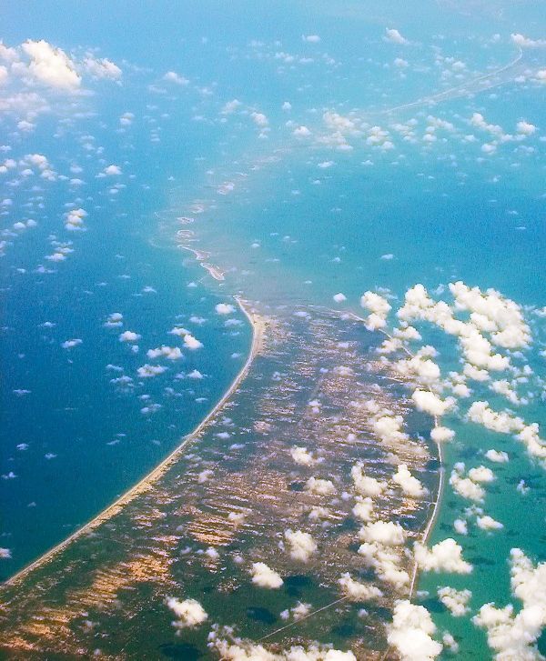 an aerial view of the ocean and land from above, with clouds in the sky