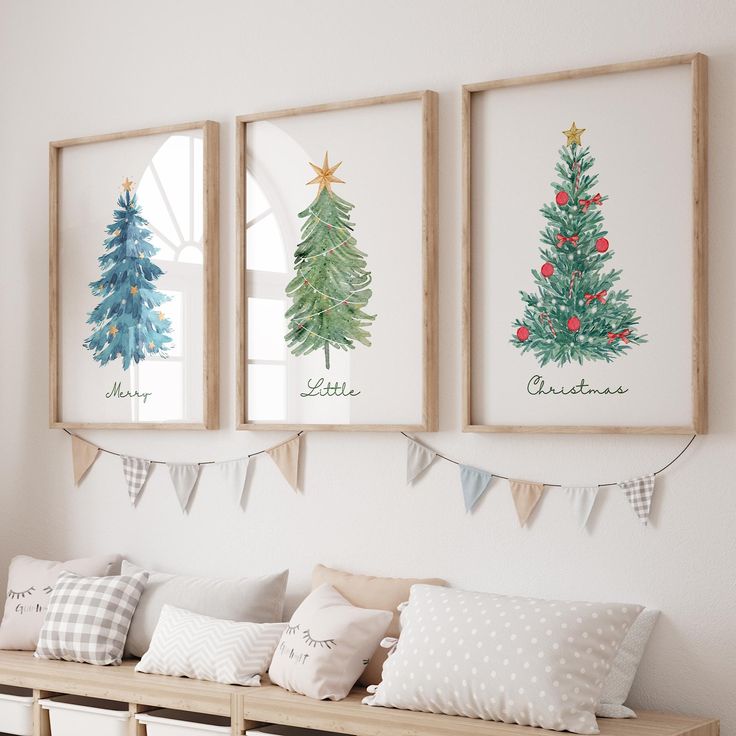 three framed christmas trees are hanging on the wall above a bench with pillows and blankets