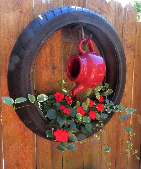 a red watering can hanging from a tire with flowers in the bottom and on top