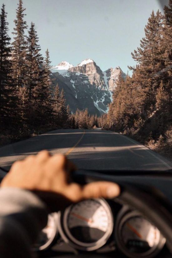 a person is driving down the road with mountains in the backgrouund and trees on both sides