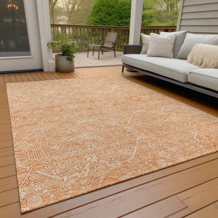 an orange rug on a wooden deck in front of a house with a couch and chair