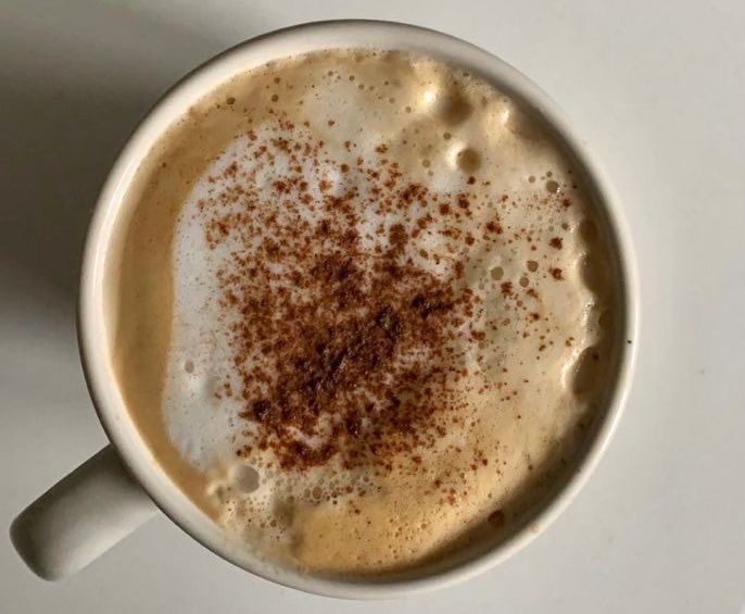 a cup of coffee with cinnamon sprinkles in it on a white table