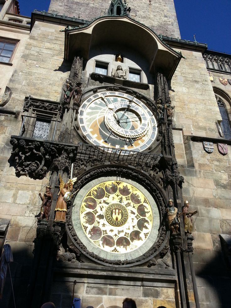 two clocks on the side of a building with people standing in front and looking at them