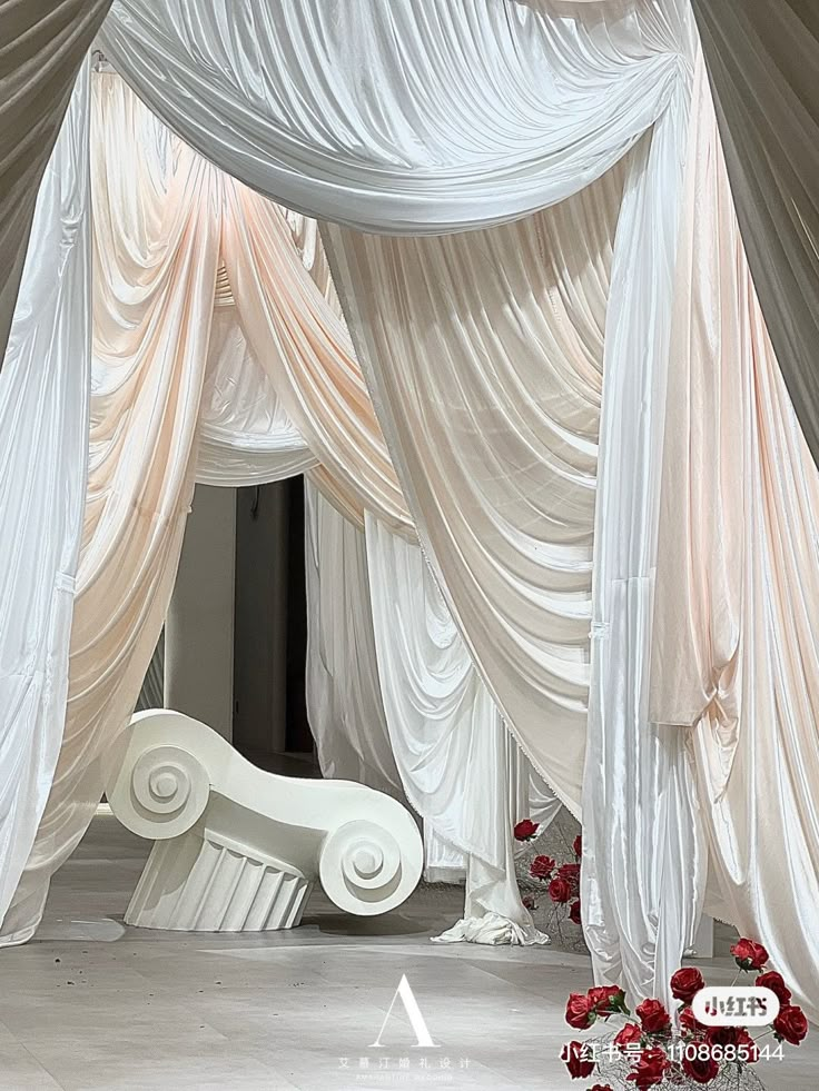 a white bed covered in draping and flowers on top of a floor next to a wall