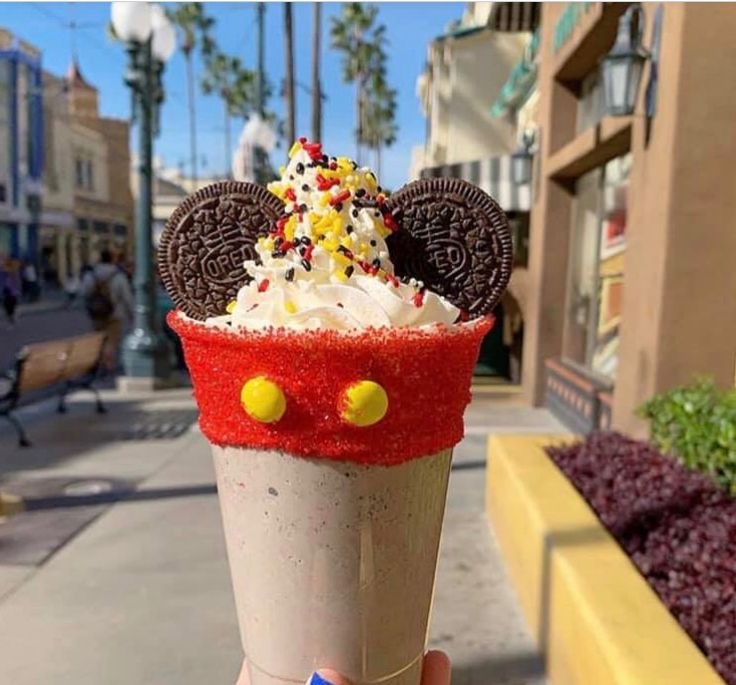 a person holding up a cup with ice cream and oreo cookies on it in front of a building