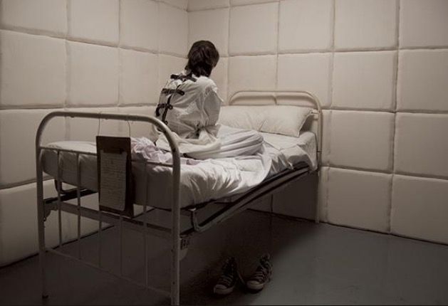 a woman sitting on top of a metal bed in a room with white tile walls