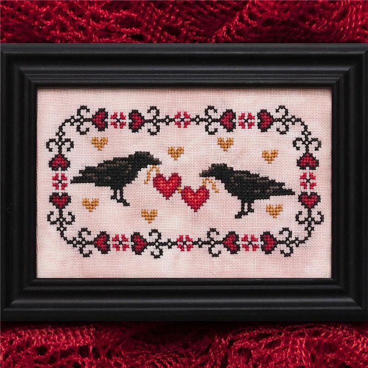 two black birds in a heart frame with hearts on the bottom and red fabric behind them