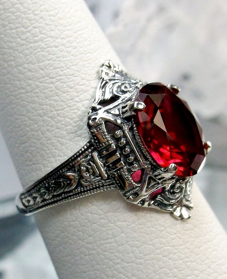 Simulated Red Ruby Ring Cleopatra Design#209 Custom Made To Order   This is a stunning Art Deco reproduction ring in sterling silver. The flawless simulated oval full cut red ruby gemstone is 10mm x 8mm. The setting is 18mm North to South on the finger. The inside of the band is marked 925 for solid sterling silver. The beautiful filigree is a mixture of Egyptian Revival and Art Deco design. There is   lovely swirl patterns in the geometric design.  Take an imaginary trip down the Nile river and Antique Oval Red Ruby Ring, Victorian Style Red Round Rings, Antique Red Ruby Gemstone Ring, Antique Red Ruby Ring, Antique Red Ruby Ring For Anniversary, Ornate Round Red Ruby Ring, Antique Round Red Ruby Ring, Vintage Red Ruby Ring With Intricate Design, Antique Red Ruby Ring For Wedding