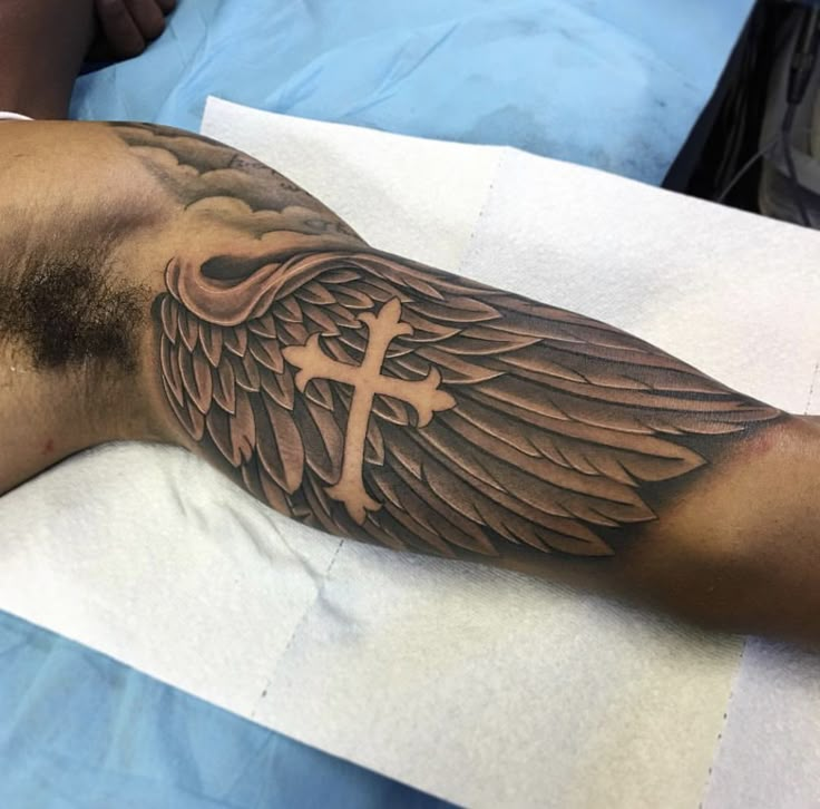 a man with a cross and wings tattoo on his arm