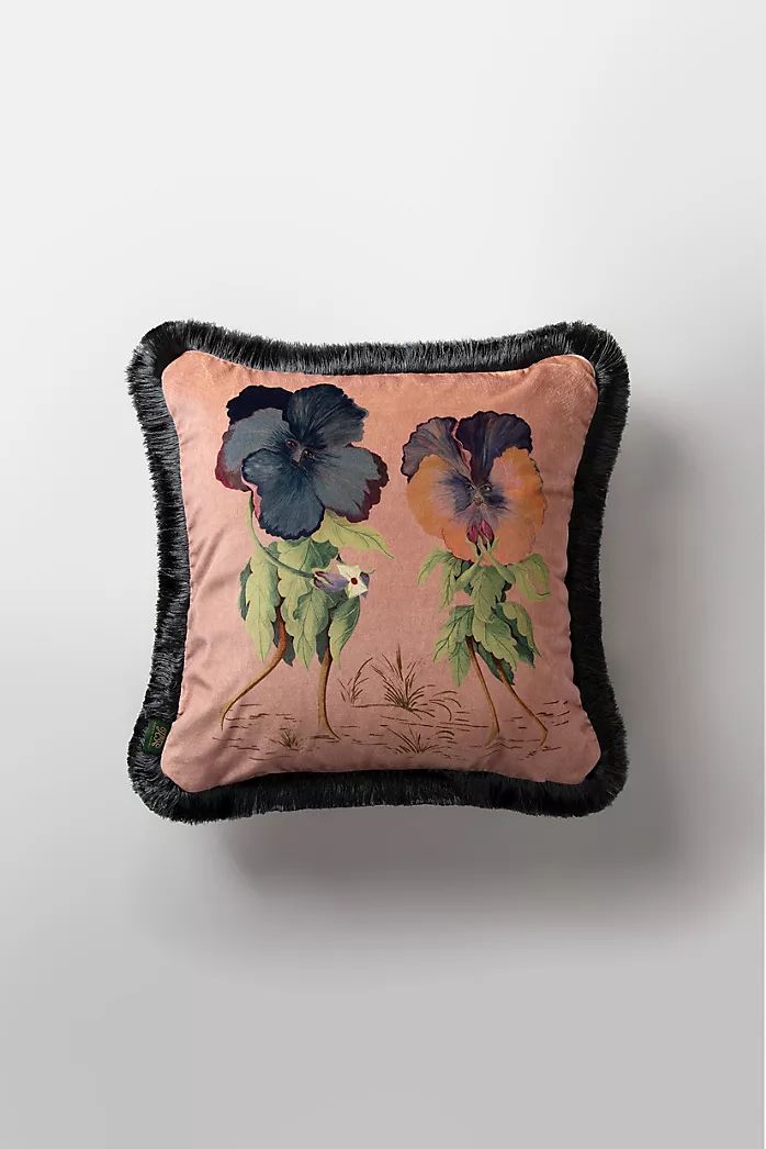 a pink pillow with black trim and flowers on the front, sitting against a white wall