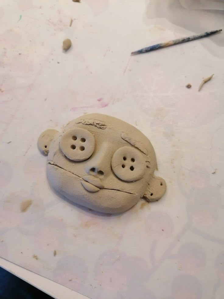 a clay face sitting on top of a table next to a pair of crayons