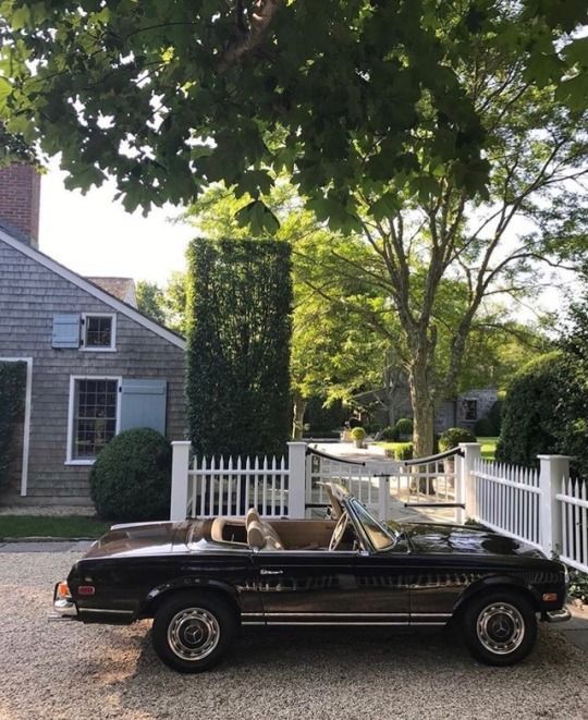 an old car parked in front of a white picket fence