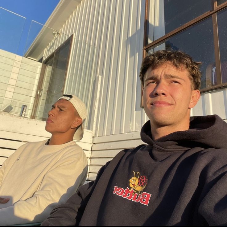 two young men sitting next to each other in front of a white building with windows