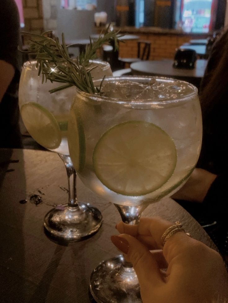 two gin cocktails with lemon and rosemary garnish sit on a bar top