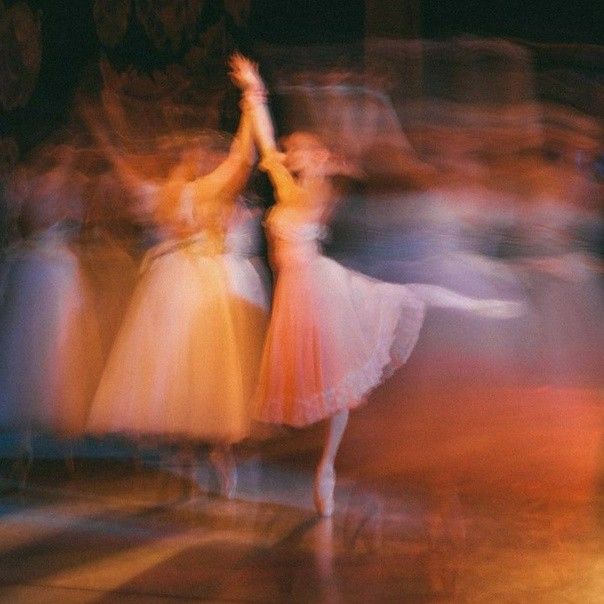 blurry photograph of dancers in motion on stage at an event or show, with people dressed in white and pink dresses