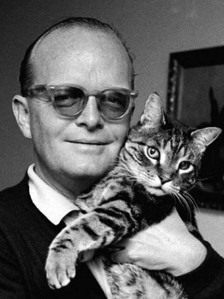 a man holding a cat in his arms and smiling at the camera while wearing glasses