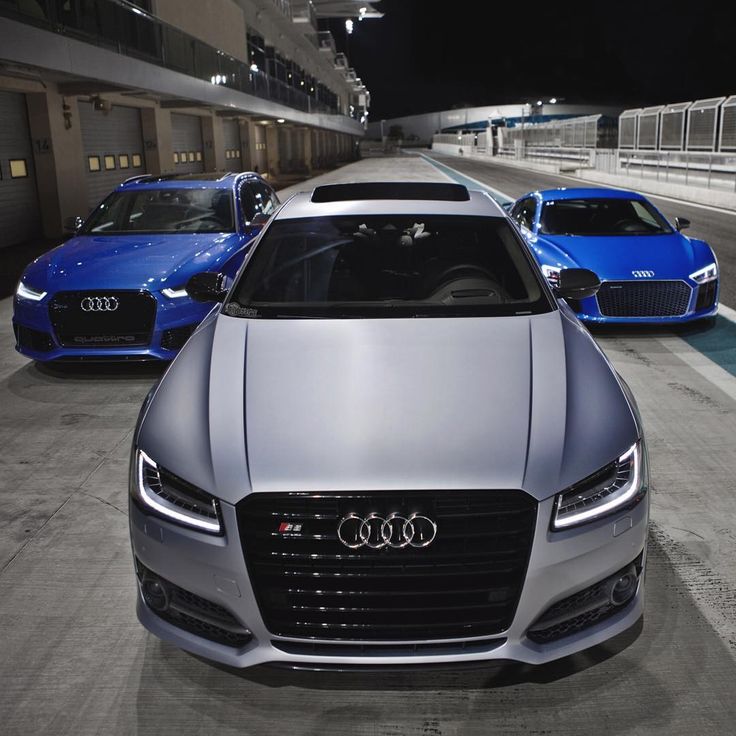 three different colored cars parked next to each other in front of a building at night