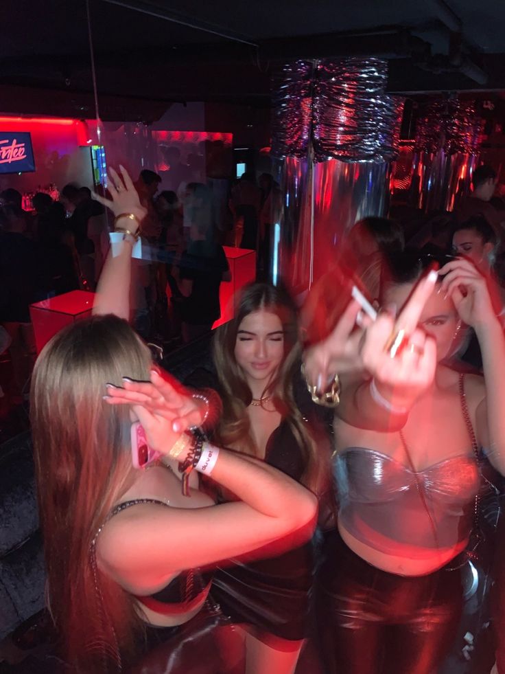 two women in leather outfits dancing at a party with their hands up and one woman holding her phone