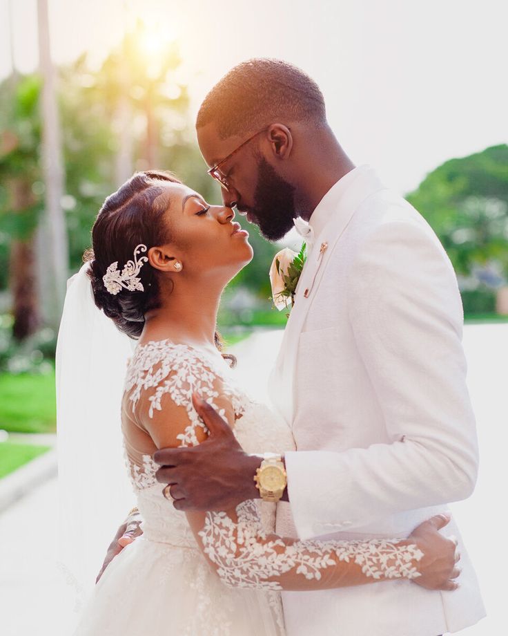 a bride and groom kissing in front of the sun on their wedding day, dressed in white