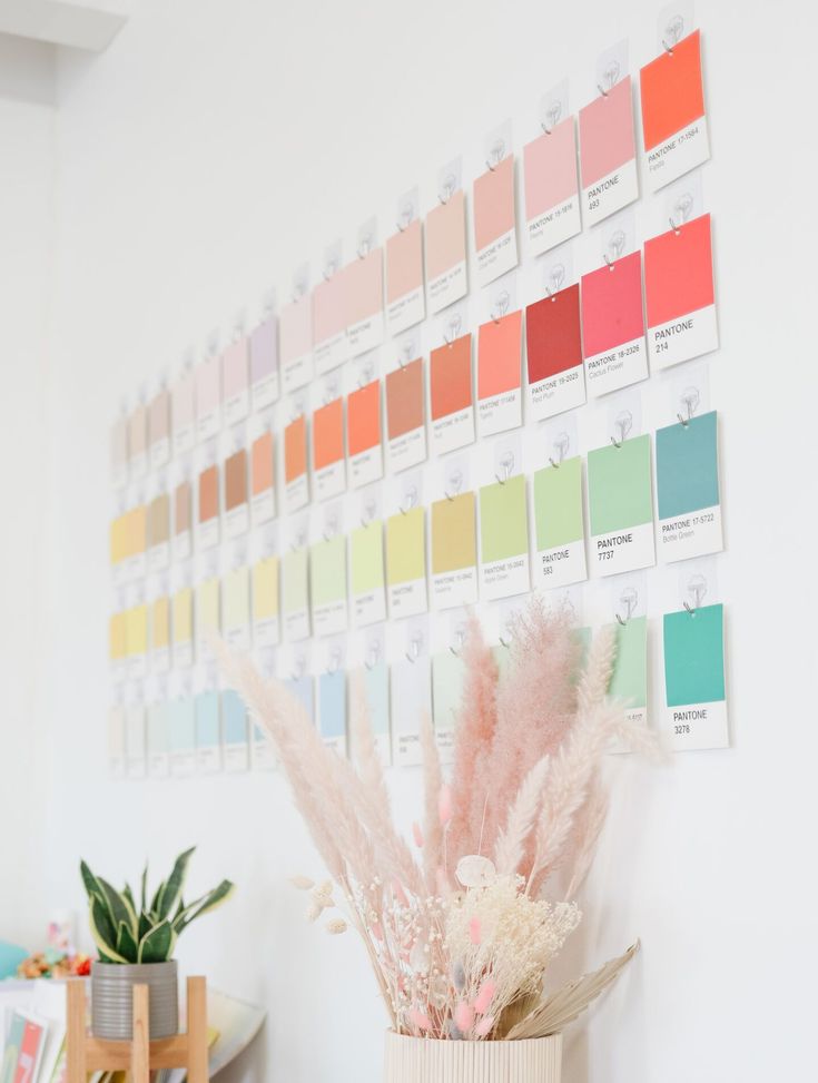 a vase filled with lots of pink flowers next to a wall covered in color swatches