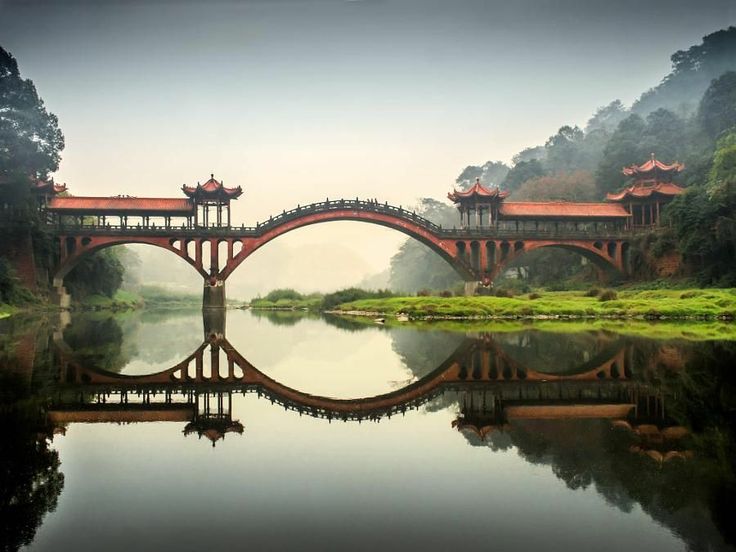 a bridge over a body of water with trees in the background and foggy sky