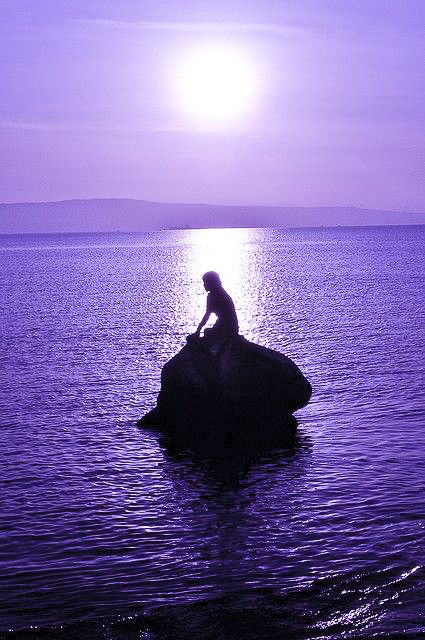 a person sitting on top of a rock in the water