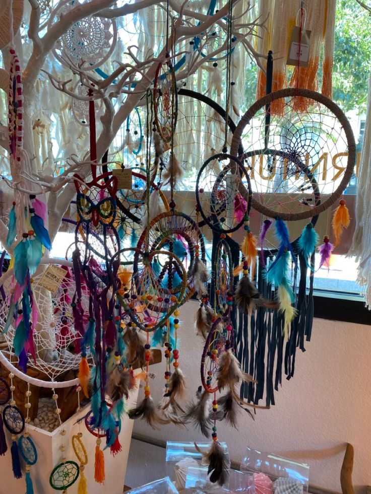 an assortment of colorful dream catchers hanging from a tree in front of a window