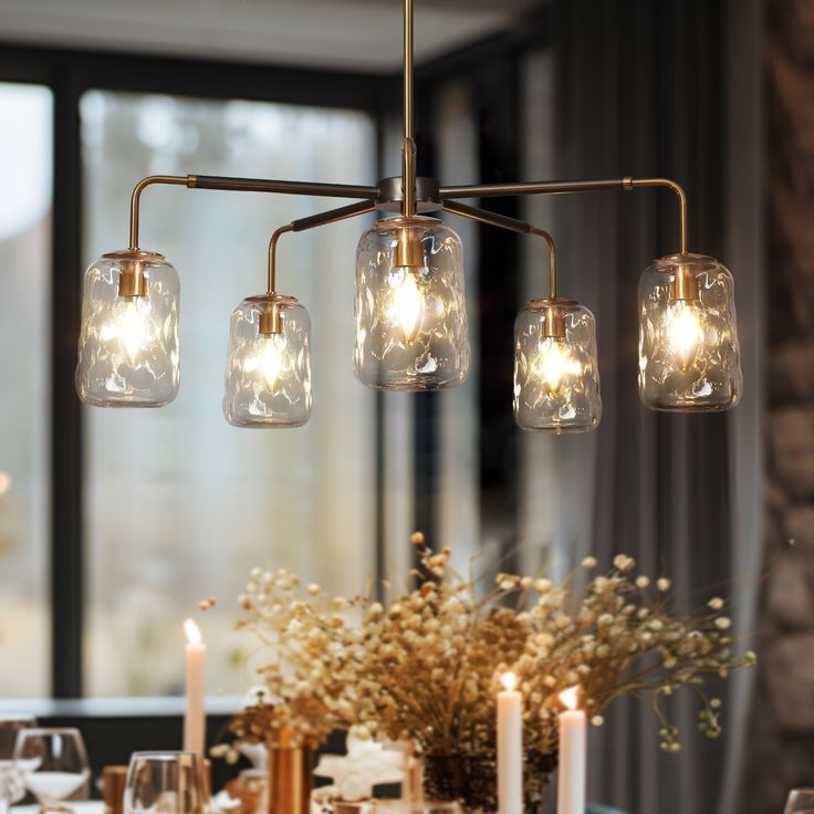 a chandelier hanging over a dining room table with candles and flowers on it