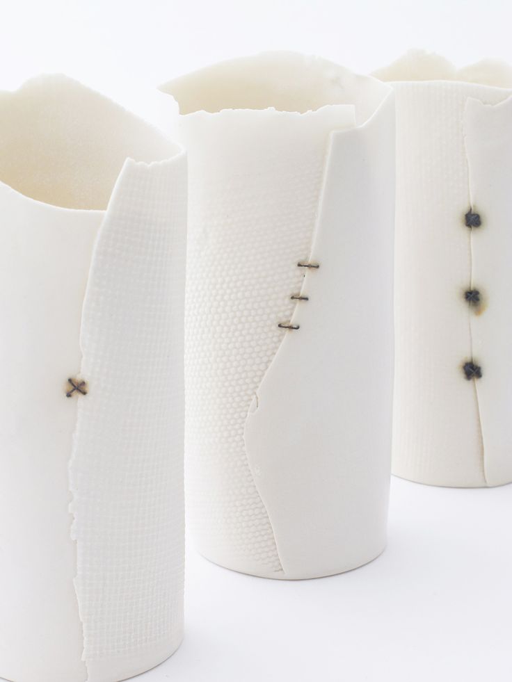 three white vases with black beaded details on the handles and sides, all lined up against one another