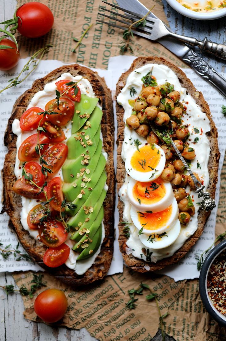 two pieces of bread with eggs, avocado and tomatoes on it next to other food