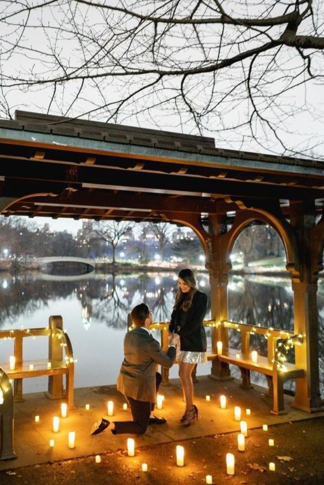 two people sitting on a bench in front of a lake with lit candles around them