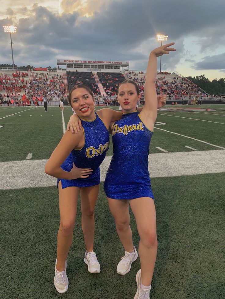 two cheerleaders posing for the camera at a football game