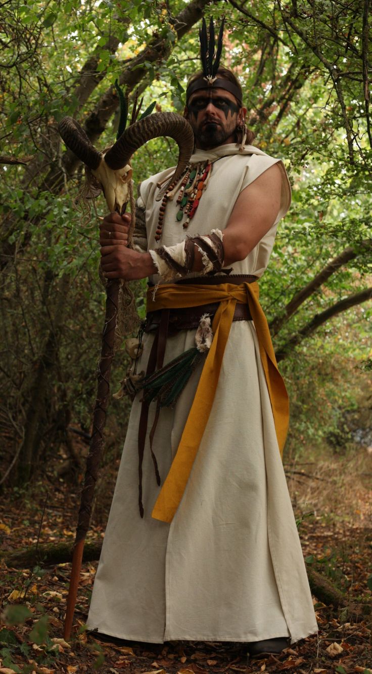 a man dressed in native american clothing and holding an animal's tail while standing in the woods