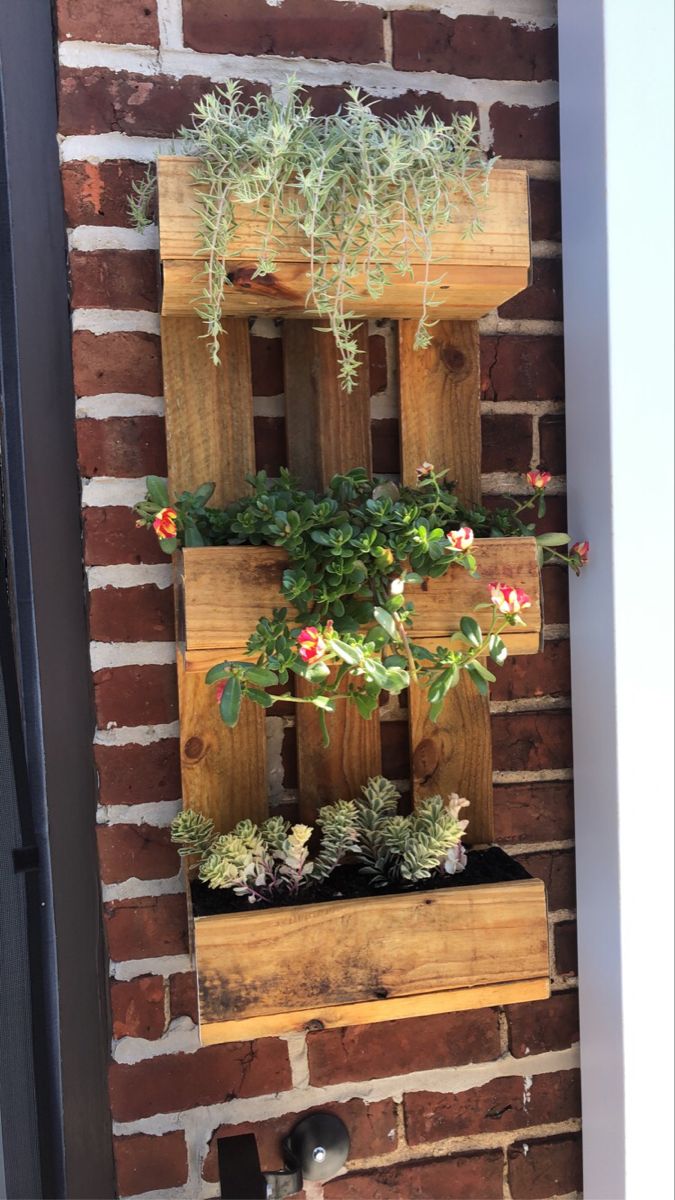 a wooden planter with succulents and flowers in it on a brick wall