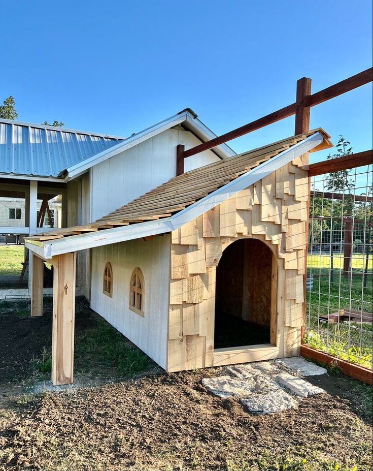 a dog house built into the side of a fenced in area with grass and dirt