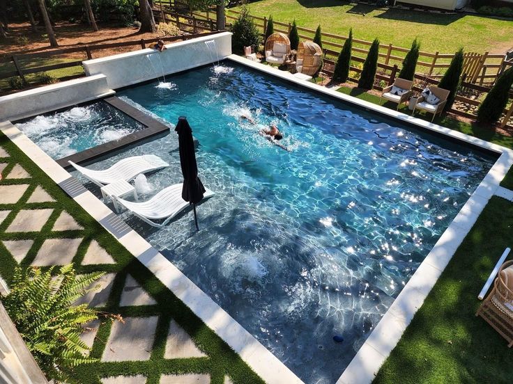 an aerial view of a swimming pool with people in the water and lawn chairs around it