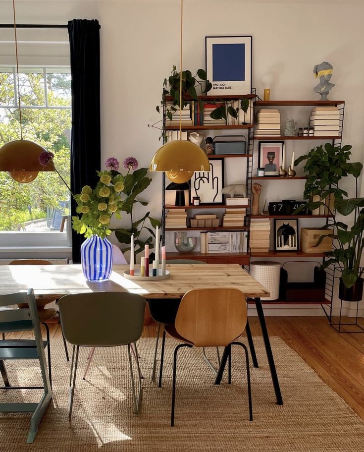 a dining room table and chairs in front of a bookshelf filled with plants