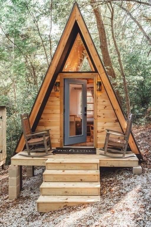 a small cabin in the woods with stairs leading up to it's front door