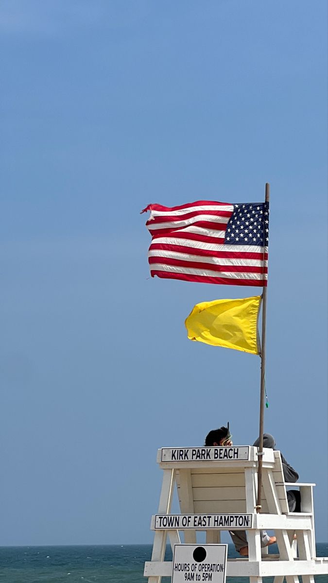 a lifeguard tower with an american flag on top and yellow flags flying above it