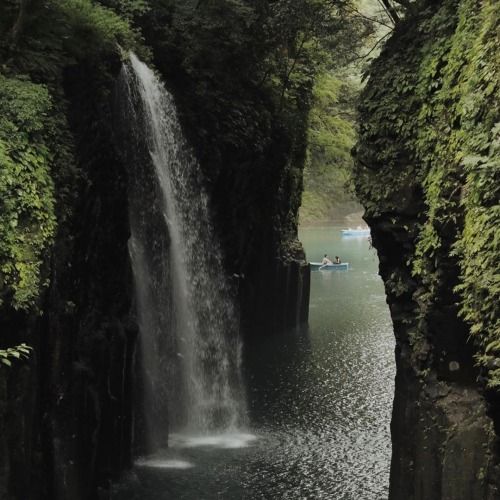 there is a waterfall in the middle of some water and people on boats below it