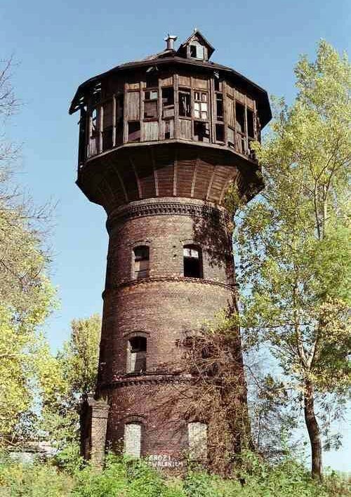 an old water tower sitting on top of a lush green hillside next to trees and bushes