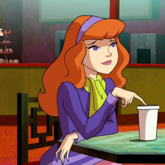 a woman with red hair sitting at a table holding a cup and pointing to the side